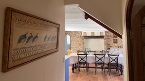Zona pranzo con tavolo e sedie, una scala e un muro di pietra sullo sfondo.