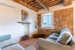 A cozy living room with a stone wall, a fireplace, a window with a view, and a sofa. - Podere il Leccio with a Pool (LUCCA)