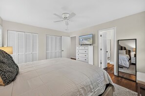 Une chambre à coucher comprenant un lit, un ventilateur de plafond, une télévision et une armoire.