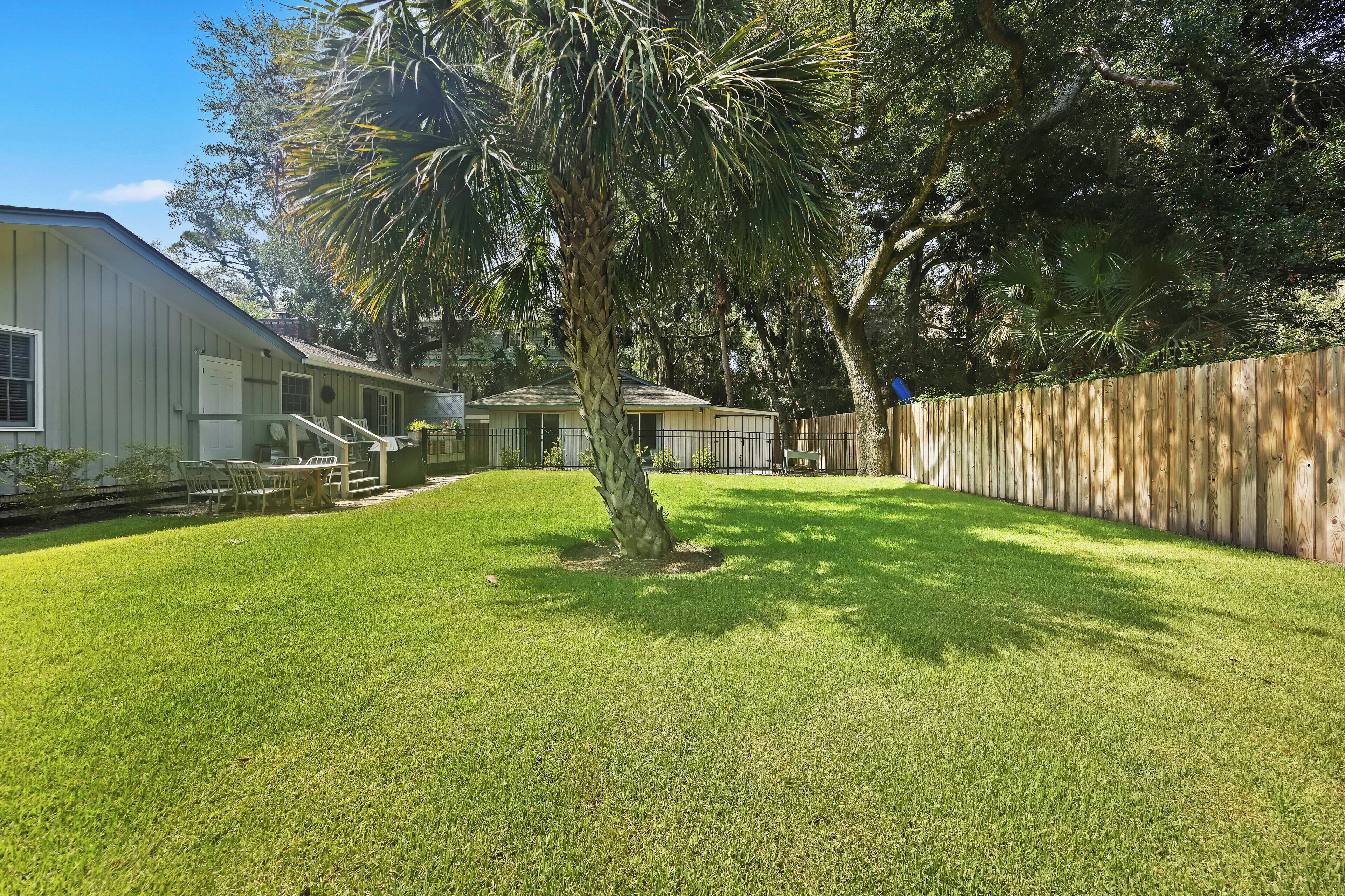 Um quintal residencial com gramado, cerca de madeira e uma casa com varanda.