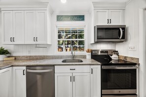 A modern kitchen with white cabinetry, a stainless steel dishwasher, a built-in oven, and a microwave. - 10 Myrtle Lane - South Forest Beach! (Hilton Head)
