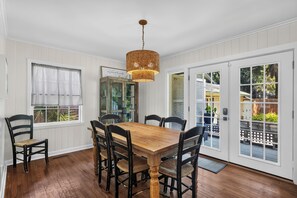 A dining area with a wooden table and chairs, a hanging light fixture, and a view through a glass door to an outdoor deck. - 10 Myrtle Lane - South Forest Beach! (Hilton Head)