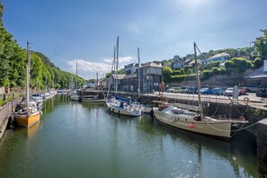 A marina with multiple boats docked, a building with signage, and a hillside with houses in the background. - Felinheli Holiday Cottage with Panoramic Views of the Menai | Angorfa (Felinheli)