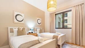 Ein Hotelzimmer mit zwei Betten, einem großen Fenster mit Vorhängen und Kunstwerken an den Wänden.