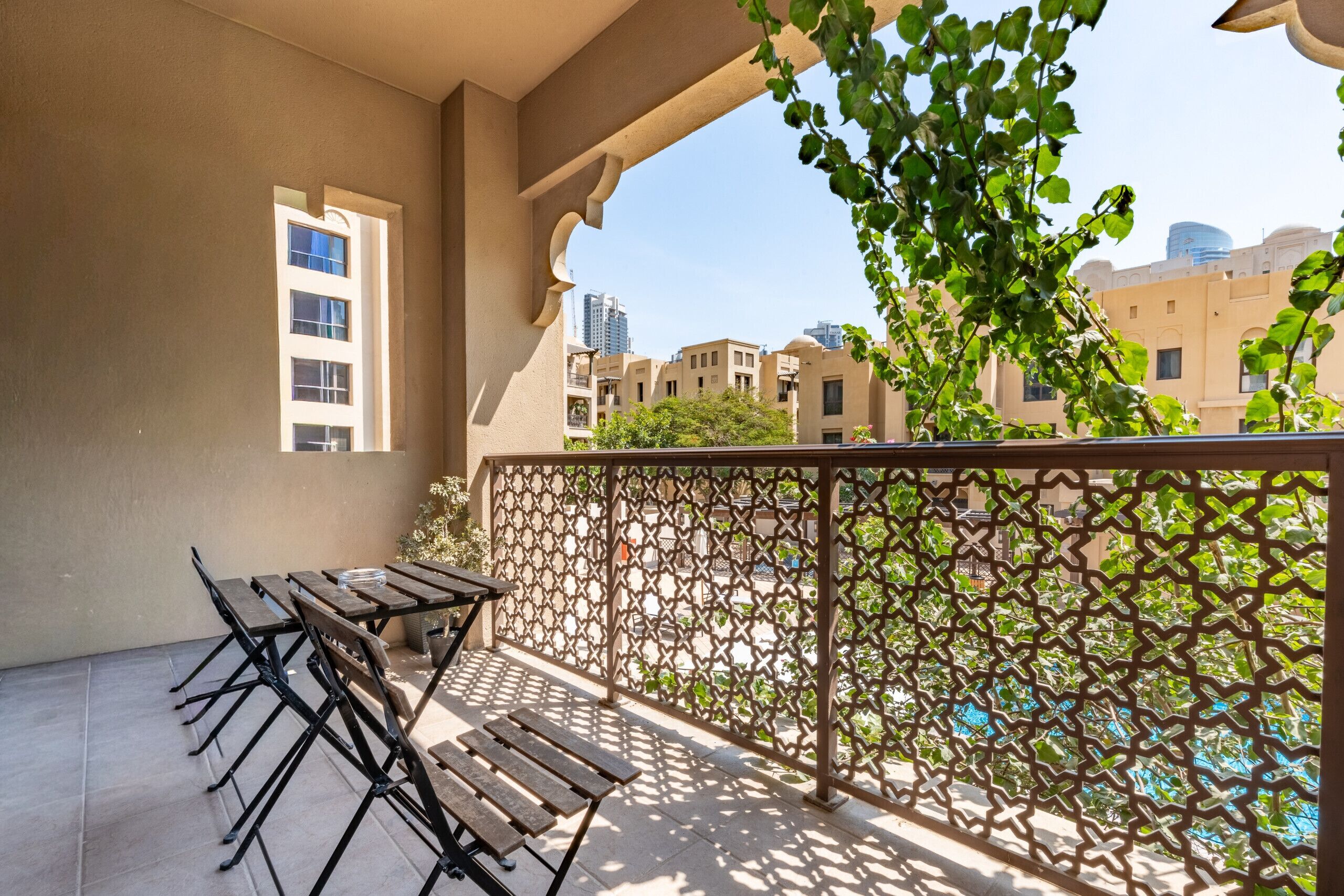 Un balcón con una mesa y sillas, una verja decorativa y vistas a edificios y una piscina.