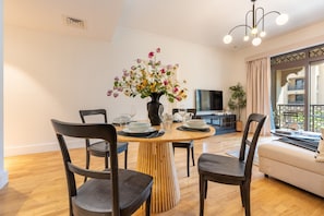 A modern living room with a dining table set for four, a sofa, a TV, and a balcony with a view. - Spacious 2BR Haven, Within Easy Reach of Burj Khalifa and Dubai Mall (Dubai)