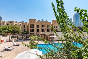 A pool area with lounge chairs and umbrellas, surrounded by buildings with balconies and a clear sky. - Spacious 2BR Haven, Within Easy Reach of Burj Khalifa and Dubai Mall (Dubai)