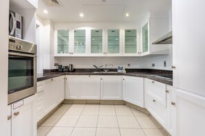 A modern kitchen with white cabinetry, a built-in oven, and a stainless steel range hood. - Spacious 2BR Haven, Within Easy Reach of Burj Khalifa and Dubai Mall (Dubai)