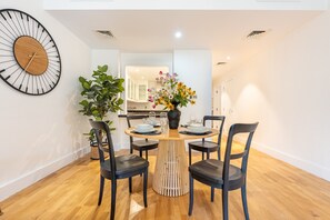 A dining area with a round wooden table, black chairs, a large wall clock, and a potted plant. - Spacious 2BR Haven, Within Easy Reach of Burj Khalifa and Dubai Mall (Dubai)