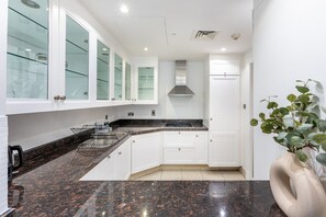 A modern kitchen with white cabinets, a granite countertop, and a stainless steel range hood. - Spacious 2BR Haven, Within Easy Reach of Burj Khalifa and Dubai Mall (Dubai)