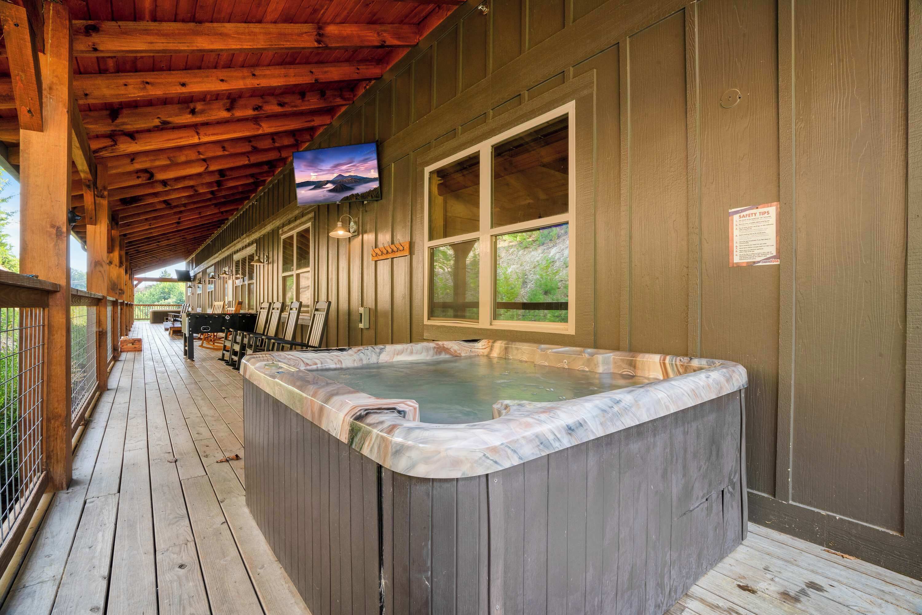 A wooden deck with a hot tub, wooden walls, and a mounted TV.