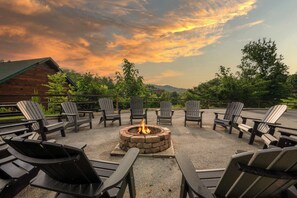 A fire pit surrounded by Adirondack chairs in a gravel area with a wooden building in the background. - Pigeon Forge Cabin Sleeps 76 | Hot Tubs, Arcade & Near Dollywood (Pigeon Forge)