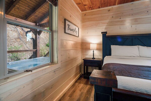 A wooden cabin bedroom with a bed, nightstand, and window. - Pigeon Forge Cabin Sleeps 76 | Hot Tubs, Arcade & Near Dollywood (Pigeon Forge)