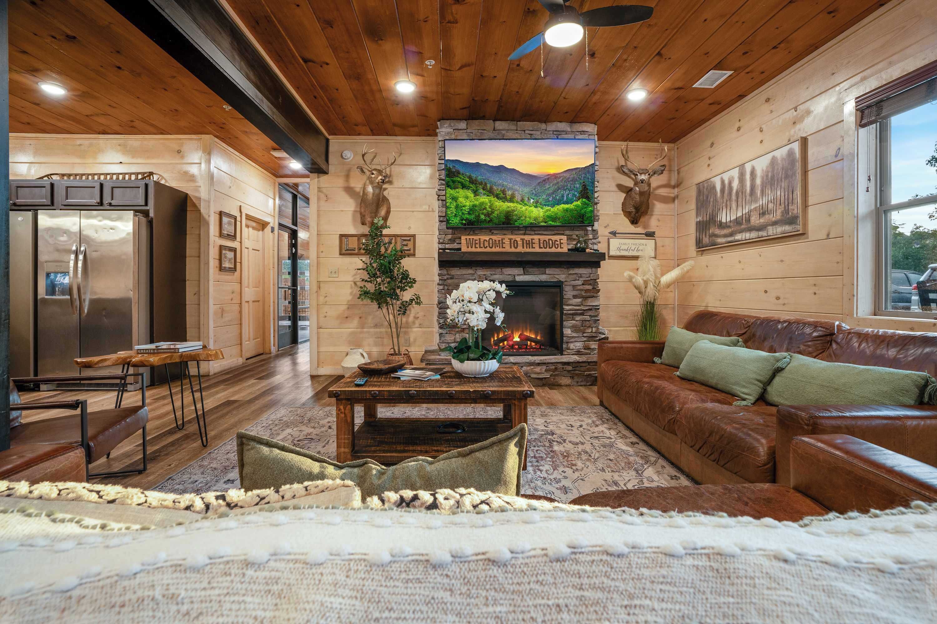 A cozy lodge interior with a stone fireplace, wooden walls, and a mounted deer head.