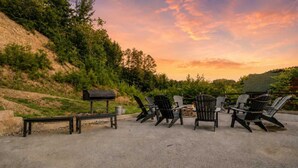 Ein Sitzbereich im Freien mit Adirondack-Stühlen und einer Bank, einem Grill und einer Feuerstelle.