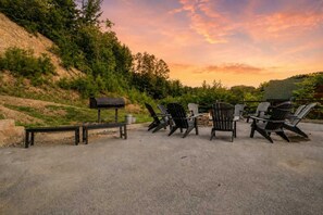 Ein Sitzbereich im Freien mit Adirondack-Stühlen und einer Bank, einem Grill und einer Feuerstelle.