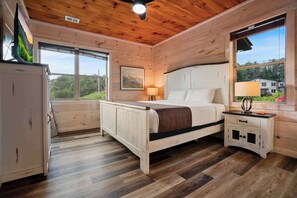A wooden cabin bedroom with a bed, bedside table, and a window. - Pigeon Forge Cabin Sleeps 76 | Hot Tubs, Arcade & Near Dollywood (Pigeon Forge)