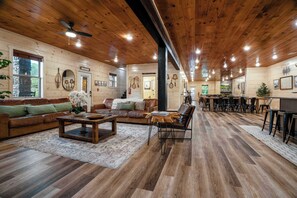 A spacious room with wooden flooring, a large sofa, a coffee table, and a dining area with chairs. - Pigeon Forge Cabin Sleeps 76 | Hot Tubs, Arcade & Near Dollywood (Pigeon Forge)