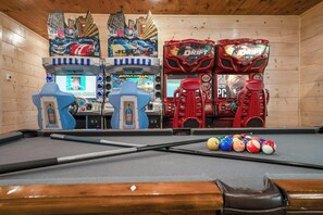 Ein Billardtisch mit Spielstock, umgeben von Spielautomaten, darunter BrawlHalla und Drift.