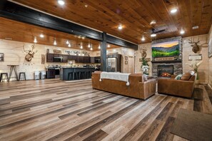 A spacious lodge interior with a kitchen, seating area, and a fireplace. - Pigeon Forge Cabin Sleeps 76 | Hot Tubs, Arcade & Near Dollywood (Pigeon Forge)