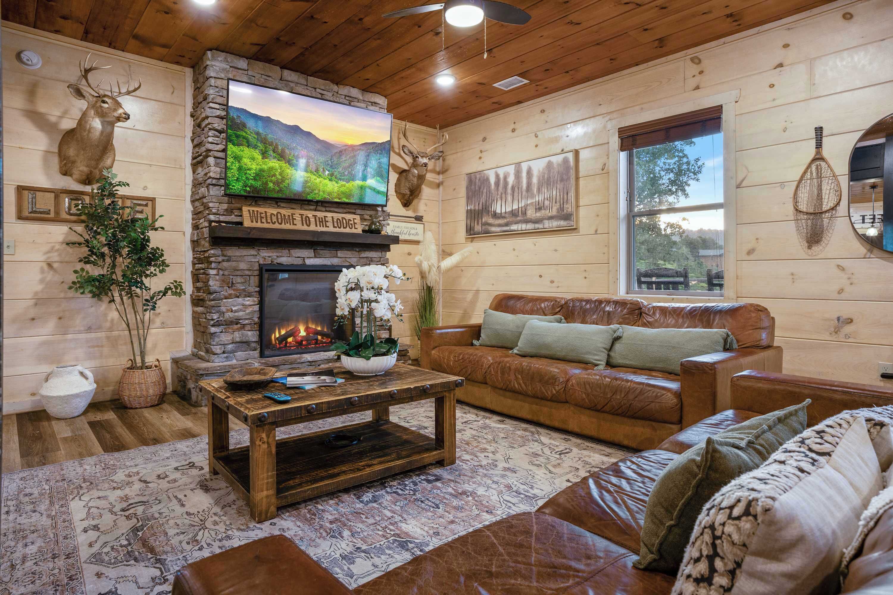 Un acogedor interior de cabaña con chimenea de piedra, sofá de cuero y televisor montado encima.