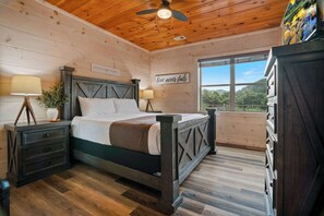 A wooden cabin bedroom with a bed, nightstands, a dresser, and a window with a view.