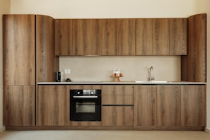 A modern kitchen with wooden cabinets, a built-in oven, and a sink. - Linum Hill Elegant 2BR Apt with Sea Views & Pool (Agios Nikolaos)