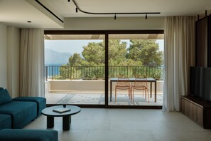 A modern living room with a sofa, a coffee table, and a balcony with a table and chairs. - Linum Hill Elegant 2BR Apt with Sea Views & Pool (Agios Nikolaos)