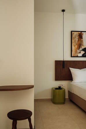 Quarto de hotel minimalista com uma cama, uma mesa redonda pequena, uma mesinha lateral verde e uma obra de arte pendurada na parede.
