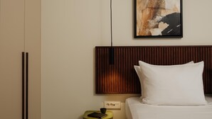 Hotellihuone, jossa on sänky, yöpöytä, seinälle ripustettu taulu ja puinen pääty.
