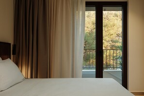 Une chambre d’hôtel avec un lit, des rideaux et une vue sur un balcon bordé d’arbres.