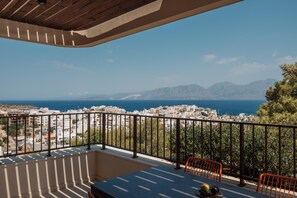 Ein Balkon mit Tisch und Stühlen, der auf eine Küstenstadt mit Bergen im Hintergrund blickt.