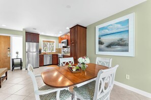 A dining area with a wooden table, white chairs, and a fruit platter.