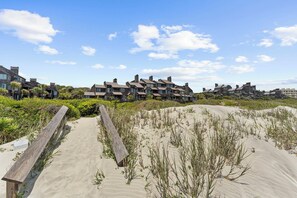 A beachfront property with multiple stone buildings, a sandy pathway, and surrounding vegetation.
