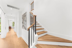 A modern staircase with wooden steps and black railings, leading to a room with a large abstract painting. - 333 Victory Bay : 4  BR, 4.5  BA House in Kiawah Island , Sleeps 10 (Kiawah Island)
