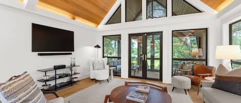 A modern living room with a large TV, comfortable seating, and a view of the outdoors.