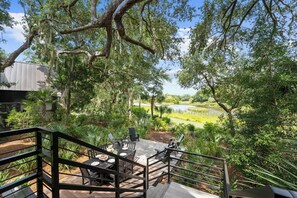 A deck with outdoor furniture overlooking a natural landscape with trees and a body of water. - Charming new Ocean Park home (Kiawah Island)