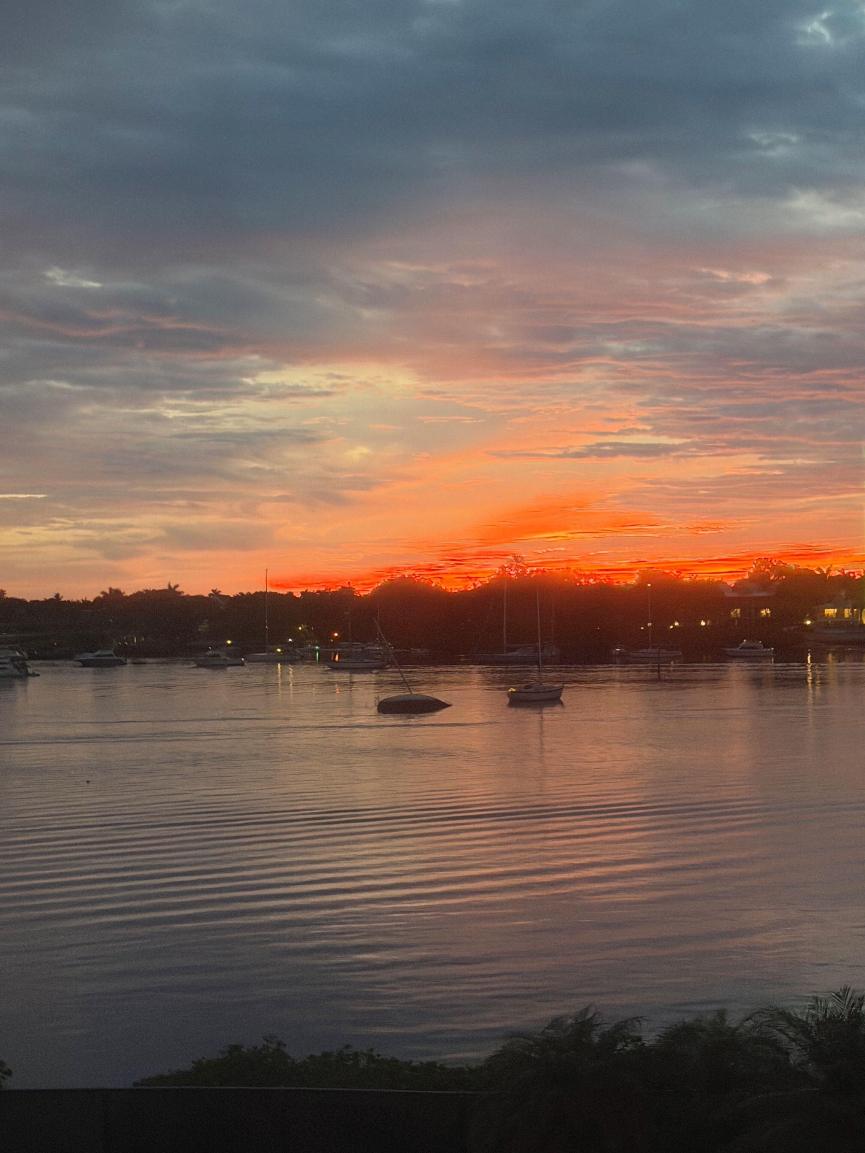 Un cuerpo de agua tranquilo con barcos y un atardecer de fondo.
