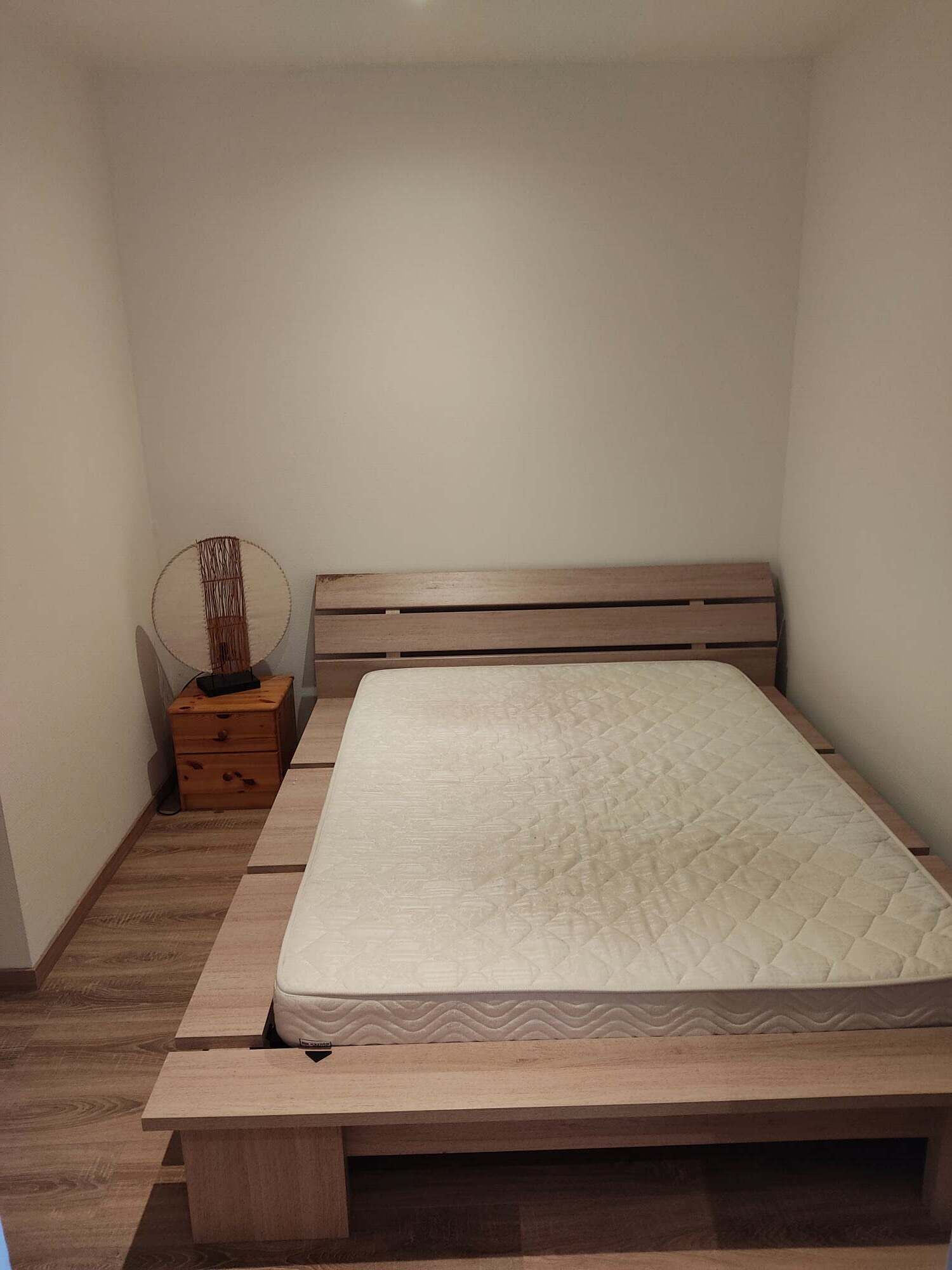 A small, single-bed room with a wooden headboard and a nightstand with a lamp.