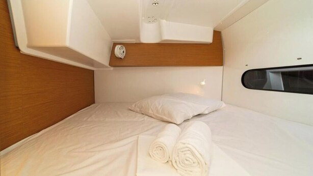 Een compacte slaapkamerhut met een houten hoofdbord, een klein raam en keurig opgerolde witte handdoeken.