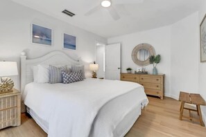 Un dormitorio con una cama grande, una mesita de noche, un aparador, un espejo y un taburete de madera.