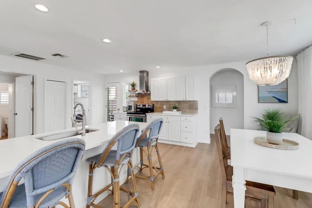 Una cocina moderna con armarios blancos, una isla central con taburetes y una mesa de comedor con sillas.
