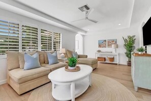 A modern living room with a beige sofa set, a white coffee table, and a ceiling fan.