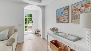 Uma sala de estar moderna com um sofá branco, um banquinho de madeira e uma lareira. Há duas obras de arte emolduradas na parede e um cesto no chão.