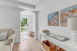Un salon moderne avec un canapé blanc, un tabouret en bois et une cheminée. Deux œuvres d’art encadrées ornent le mur, et un panier est posé sur le sol.