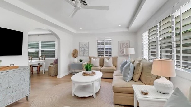 Uma sala de estar moderna com um sofá branco, uma mesa de centro e uma TV fixada na parede.
