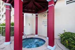 Un jacuzzi debajo de un pabellón rojo con un reloj en la pared y un letrero con las normas de la zona de la piscina.