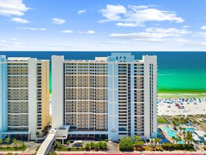 Um hotel na praia com vários edifícios altos, área de piscina e praia com guarda-sóis.