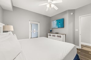 Une chambre à coucher avec un lit, une commode, un ventilateur de plafond, un téléviseur et une porte.