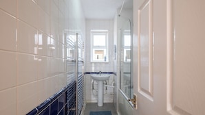 Een kleine badkamer met witte tegels, een wastafel en een douchehoek.